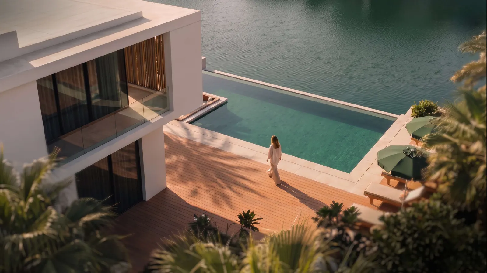 A resident walks along a timber deck beside an infinity pool that meets the canal