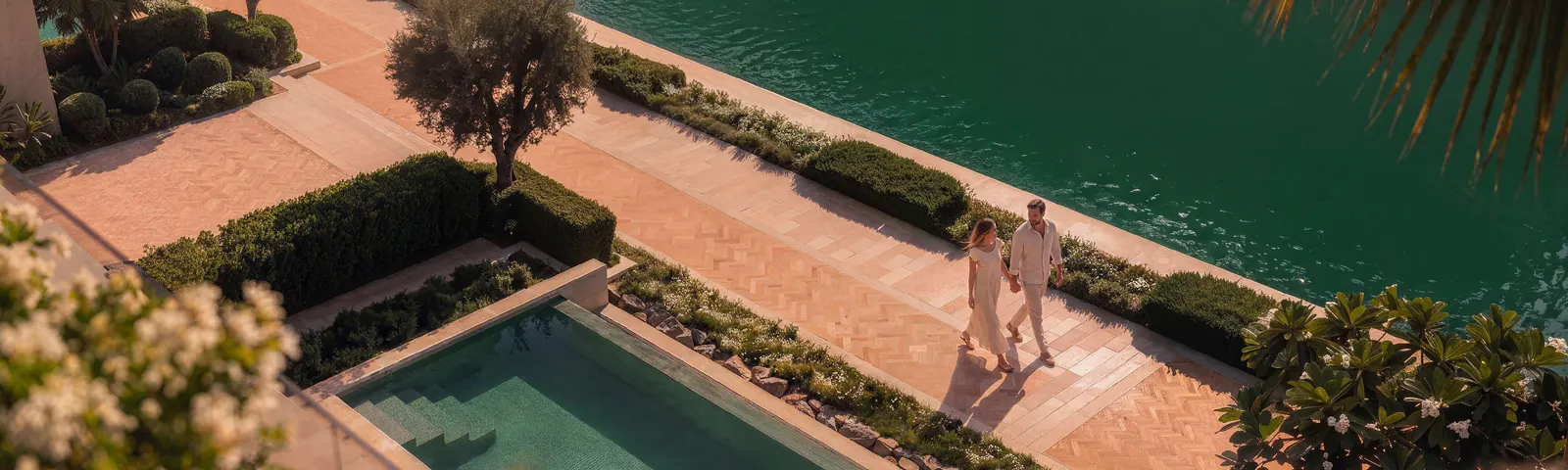 A couple walks the herringbone canal promenade past a villa pool